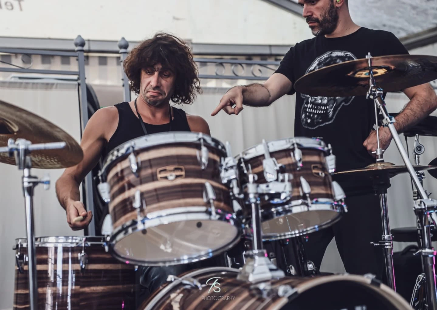 A drummer at a drum kit during a BDExhausting camp session, with another participant pointing towards the toms.