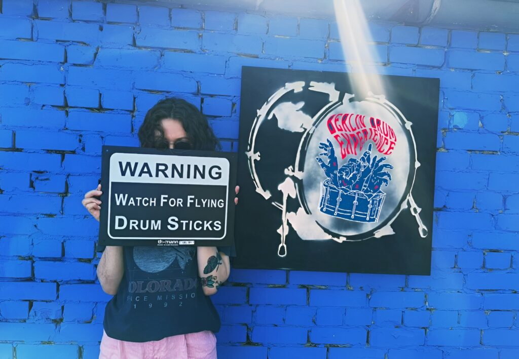 A BDE drummer holding a Watch for Flying Drum Sticks sign