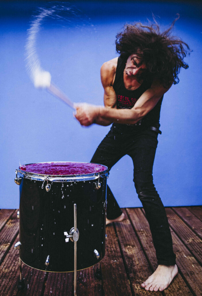 Marco throwing himself into a drum performance against a blue background
